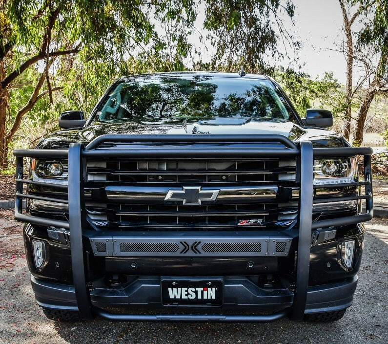 Head-on front view of a black Chevrolet Silverado fitted with a Westin Sportsman X grille guard in black, showing the wrap-around uprights, mesh punch plate and Westin-branded license plate cover