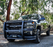 Westin Sportsman X grille guard in textured black mounted on the front of a black Chevrolet Silverado pickup parked under eucalyptus trees, shown from a front three-quarter angle