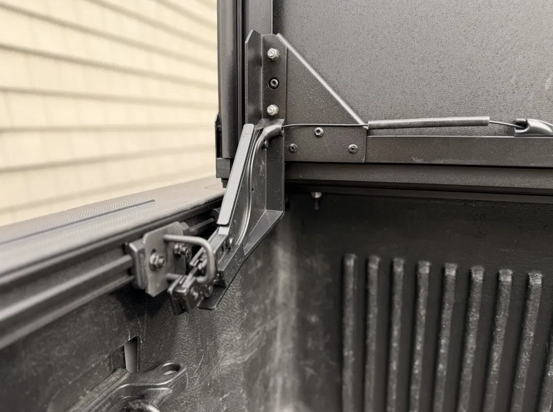 Close-up of the Worksport NEXUS hard folding tonneau cover: customer close-up of the black auto-locking arm and cable on the bed rail with the front panel upright