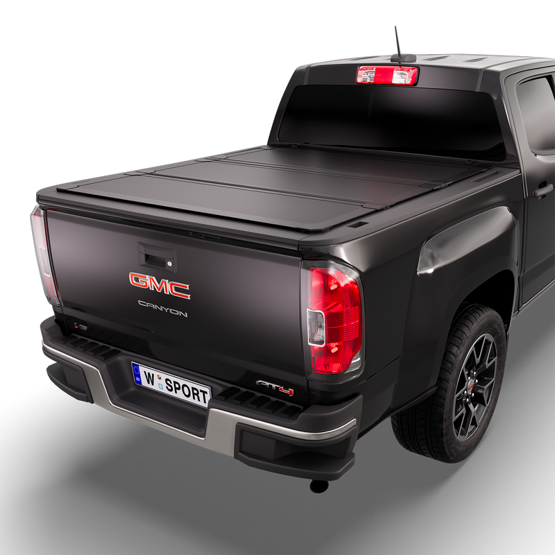 Worksport NEXUS hard folding tonneau cover on a pickup: 3D studio render of a black GMC Canyon from the rear quarter with a black NEXUS hard folding tonneau cover closed, all three panels flat over the bed