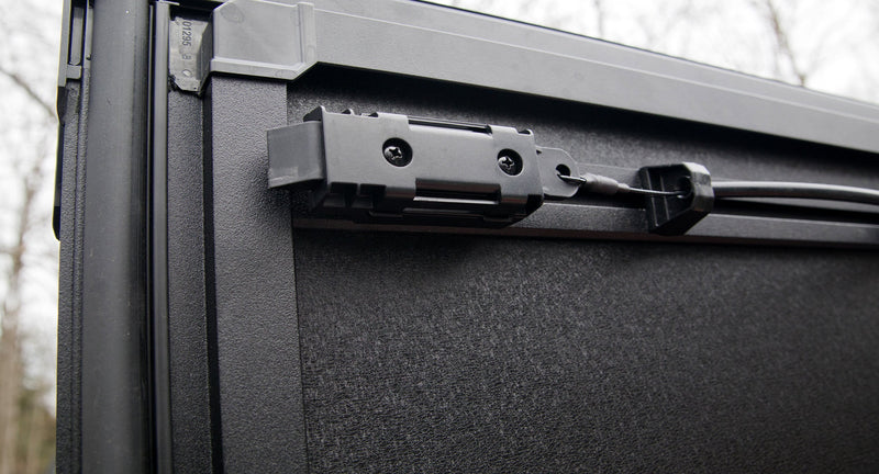 Close-up of the Worksport NEXUS hard folding tonneau cover: close-up of a black latch and release cable on the underside edge of an upright cover panel