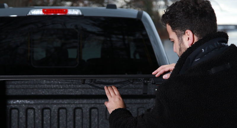 Worksport NEXUS hard folding tonneau cover on a pickup: a man in a dark jacket handles a black cover panel at the front of a pickup bed by the rear window